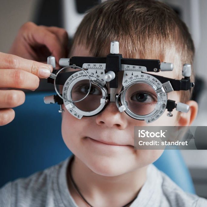 Tuning the intrument. Little boy with phoropter having testing his eyes in the doctor's office.