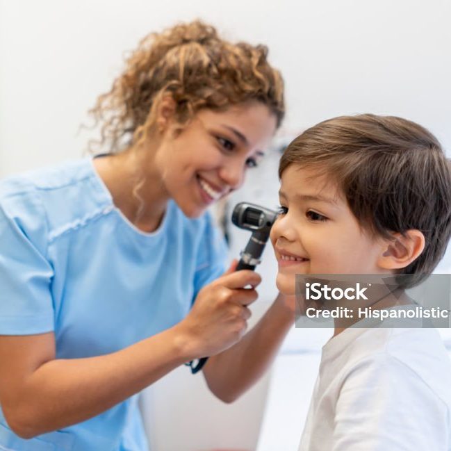 Beautiful female pediatrician checking a little boy's ears both smiling at the hospital