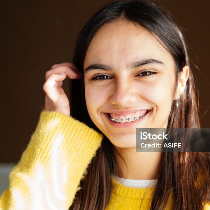 Portrait of a happy teen girl with braces and some acne smiling at home with the sun coming through the window