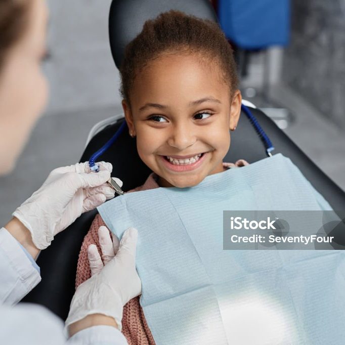 Portrait of smiling little girl in dental chair with nurse preparing her for teeth check up, copy space