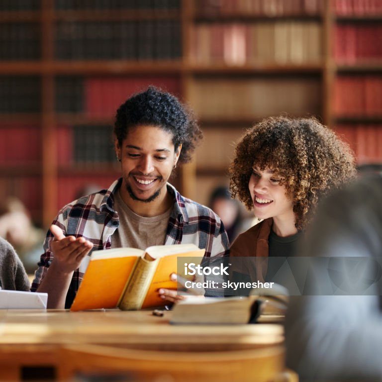 Happy diverse university couple cooperating while reading a book in library.