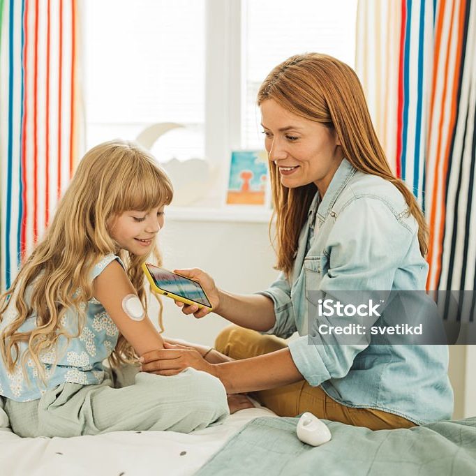 Mother checking glucose level on smart phone on daughter's glucose meter before bedtime.