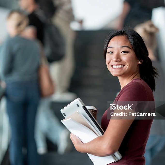 An outgoing student smiles brightly while holding a notebook on a bustling escalator, representing educational ambition and positivity.