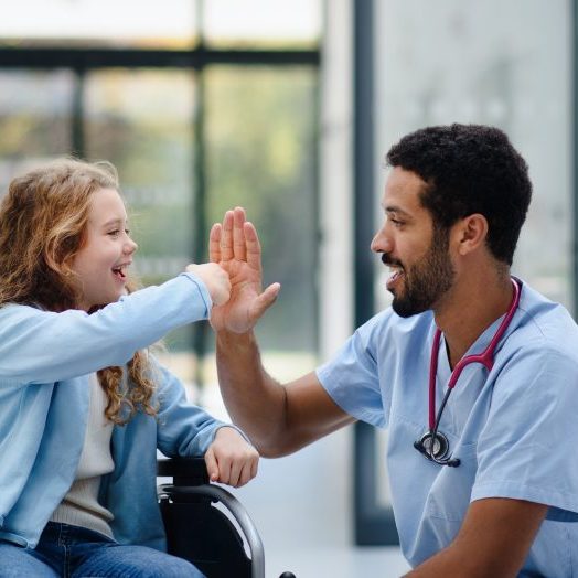 Young,Multiracial,Doctor,Having,Fun,With,Little,Girl,On,Wheelchair.